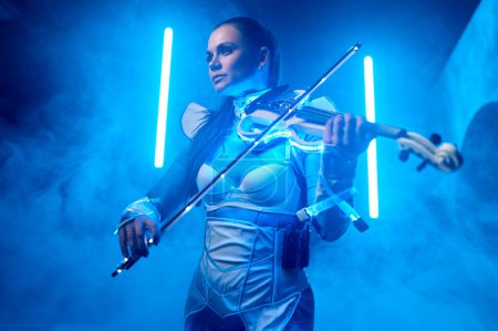 Téléchargez les photos : Belle violoniste jouant du violon électrique sur scène avec lumière au néon et fumée. Portrait de femme musicienne inspiré. Performance artistique professionnelle - en image libre de droit