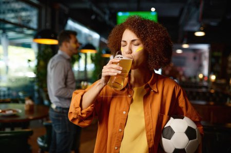 Photo for Portrait of young thirsty girl football fan drinking beer while rest and spend time with friends in sports bar - Royalty Free Image