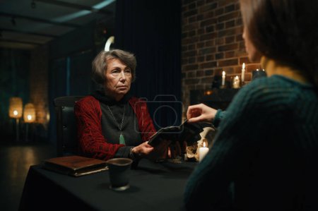 Photo for Old mature soothsayer holding divination tarot cards in front of female client. Fortunetelling concept - Royalty Free Image