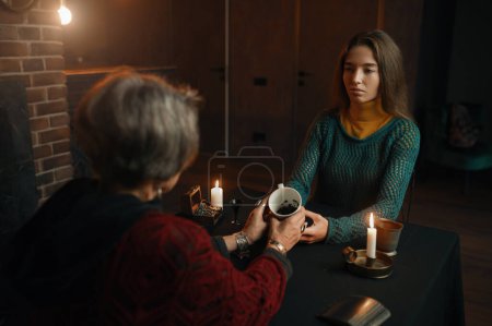 Téléchargez les photos : Jeune femme visitant sorcière tzigane pour divination sur les marc de café. Concept de la bonne aventure - en image libre de droit