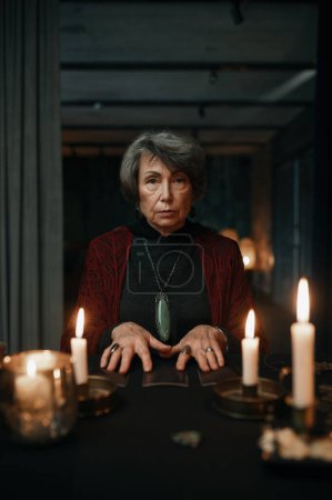Photo for Portrait of serious confident fortune teller holding crystal pendant over candle light for divination seance - Royalty Free Image