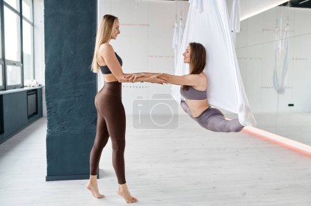 Téléchargez les photos : Woman hanging on sports hammock training leg-split with personal fly yoga instructor at fitness gym - en image libre de droit