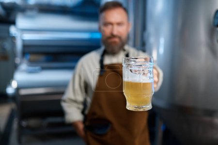 Téléchargez les photos : Freshly made craft beer in glass closeup. Brewery worker holding mug with fresh ale. Selective focus. Brewery concept - en image libre de droit