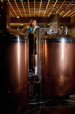 Téléchargez les photos : Mature man inspector checking craft beer at brewery. Brewer owner working at small alcohol manufacturing factory - en image libre de droit