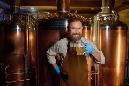 Téléchargez les photos : Senior man brewery technologist tasting fresh craft beer at microbrewery plant. Inspector working at alcohol manufacturing factory checking ale or lager - en image libre de droit