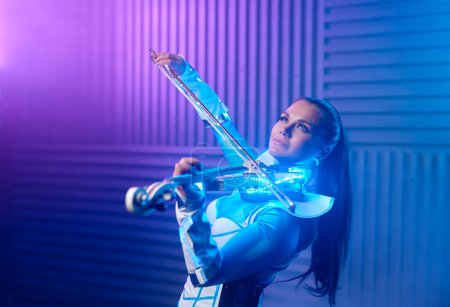 Téléchargez les photos : Portrait of talented violin solo player on stage in neon light. Beautiful woman performing music on electric fiddle - en image libre de droit