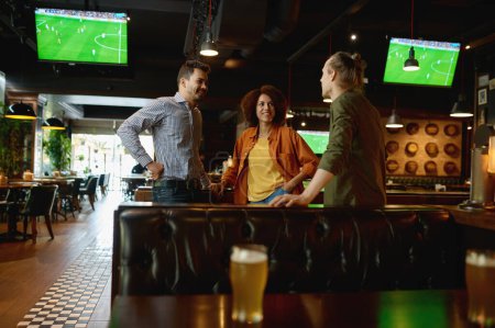 Photo for Group of happy friends resting and talking at bar or pub. Diverse interracial young people discussing football soccer match together sharing impressions - Royalty Free Image