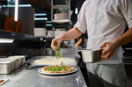 Photo for Chef sprinkling fresh greenery over traditionally made pizza. Italian fast food restaurant - Royalty Free Image
