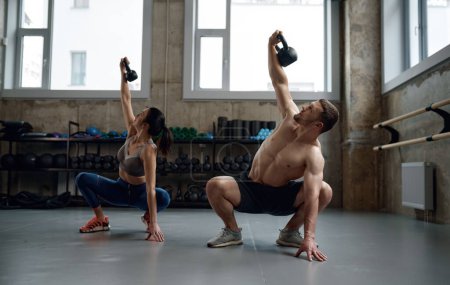 Téléchargez les photos : Man and woman with good physique holding heavy kettle bell for swing cross training hard core workout in gym. Personal class with professional sport coach - en image libre de droit