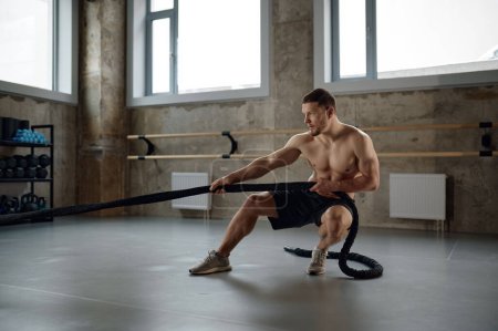 Foto de A strong man pulling training sports rope front view. Male athlete doing workout exercises at gym - Imagen libre de derechos
