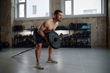 Foto de El hombre fuerte se prepara para levantar pesas pesadas entrenando con barra. Hombre muscular bombea los músculos de su brazo en el gimnasio - Imagen libre de derechos