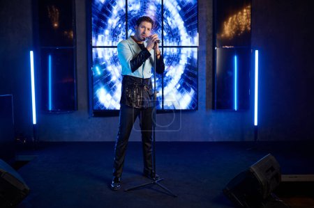 Foto de Retrato de larga duración de guapo cantante atractivo cantando en micrófono en escenario iluminado en discoteca - Imagen libre de derechos