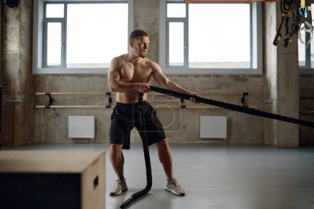 Photo for A strong man pulling training sports rope front view. Male athlete doing workout exercises at gym - Royalty Free Image