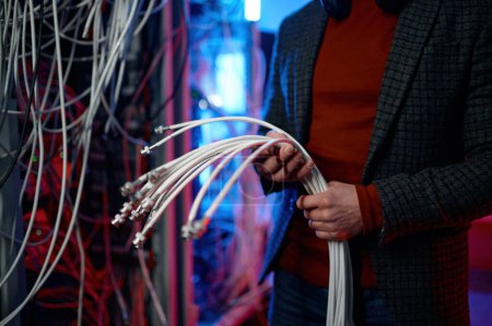 Closeup view of IT man with bunch of cables in hands while working at network server room. Engineer setting farm of mining cryptocurrency