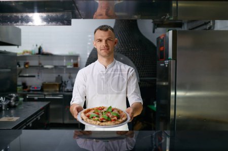 Photo for Male pizzaiolo presenting freshly cooked pizza. Cooking school master class or Italian fast food restaurant presentation - Royalty Free Image