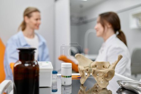 Photo for Selective focus on pelvis structure and pills on table in gynecologist office. Doctor and patient on background - Royalty Free Image