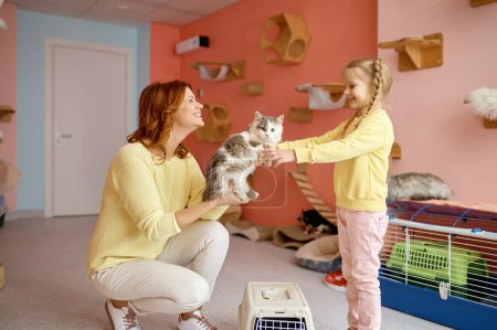 Foto de Amistosa mujer sonriente dando gato a niña sobre animal refugio fondo. Concepto de niños y mascotas - Imagen libre de derechos