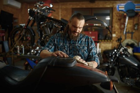 Foto de Motociclista limpiando su moto en taller de reparación el fin de semana. taller o taller de mantenimiento y reparación de máquinas de hombre barbudo - Imagen libre de derechos