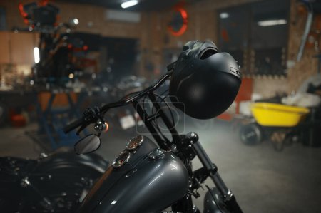 Foto de Moto con casco colgante en volante estacionado en garaje para motociclistas o taller de servicio - Imagen libre de derechos