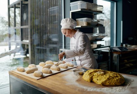 Téléchargez les photos : Boulanger femme portant l'uniforme engagé dans la fabrication de petits pains à la levure traditionnelle avec du fromage - en image libre de droit