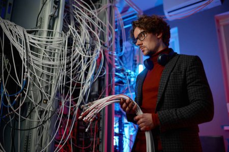 Foto de Hombre de TI con un montón de cables en las manos mientras trabaja en la sala de servidores de red. Ingeniero de ajuste de granja de la minería criptomoneda - Imagen libre de derechos