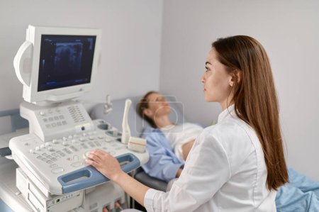 Selective focus doctor doing ultrasound of fetus to pregnant woman in modern prenatal clinic office