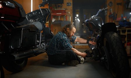 Foto de Hombre maduro motociclista reparación de motocicletas en el garaje por la noche. Mecánico de motos en el trabajo - Imagen libre de derechos