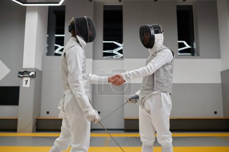 Photo for Professional fencers shaking hand after or before fencing match. Athletes in uniforms protective helmet mask greeting or thanking each other at martial art lesson - Royalty Free Image