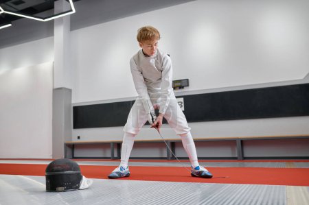 Photo for Teenage boy wearing fencing costume checking strength of blade before training or competition. Sport and hobby concept - Royalty Free Image