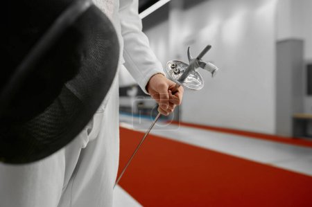 Photo for Selective focus on protective fencing mask and sword in hand of young fencer. Cropped shot of swordsman wearing uniform. Training or competition concept - Royalty Free Image