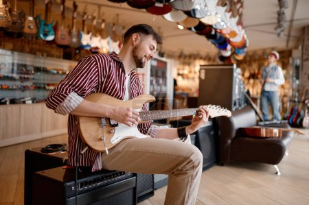Foto de Compra de equipos de audio en tienda de música. Hombre disfrutando del sonido mientras toca la guitarra conectado al amplificador - Imagen libre de derechos