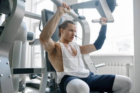 Téléchargez les photos : Sportif masculin énergique travaillant les bras pompant les muscles sur les appareils d'entraînement à la salle de sport - en image libre de droit