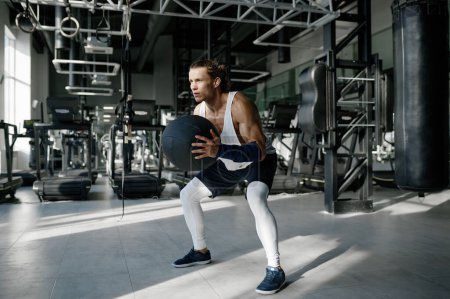 Téléchargez les photos : Sportif sportif en vêtements de sport faire squats avec des boules de médecine à la salle de gym. Concept de conditionnement physique et mode de vie sain - en image libre de droit