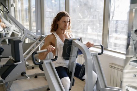 Foto de Retrato de deportista de entrenamiento duro haciendo ejercicio en la máquina de gimnasia. Culturista sensación de tensión en los músculos haciendo fuerza y empujando los brazos hacia adelante - Imagen libre de derechos