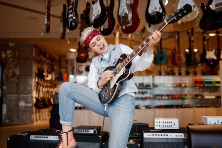 Foto de Emocional hipster mujer rockero tocando la guitarra conectado al amplificador de sonido estéreo sensación satisfacción y admiración del sonido - Imagen libre de derechos