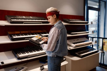 Photo for Young hipster woman holding and playing electronic mini piano at music shop store. Purchase at musical workshop sound studio concept - Royalty Free Image