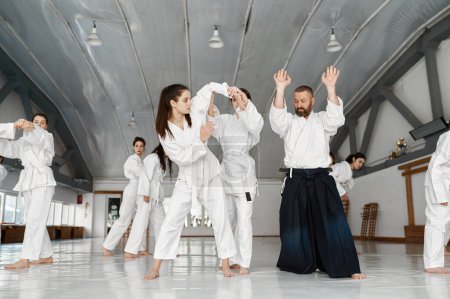 Téléchargez les photos : Adolescentes groupe d'étudiants ayant combat aikido sous le contrôle de l'instructeur. Concept de sport et d'entraînement professionnel - en image libre de droit
