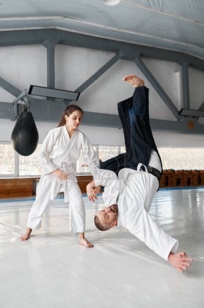 Photo for Talented female student throwing aikido teacher on floor during sparring and self defense training in gym - Royalty Free Image