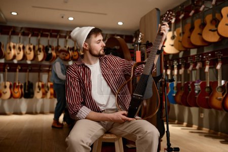 Foto de Joven hombre eligiendo una guitarra eléctrica. Guitarrista milenario comprando nuevo instrumento en la tienda de música - Imagen libre de derechos