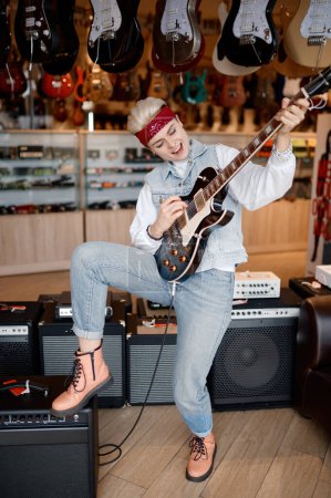 Foto de Emocional hipster mujer rockero tocando la guitarra conectado al amplificador de sonido estéreo sensación satisfacción y admiración del sonido - Imagen libre de derechos