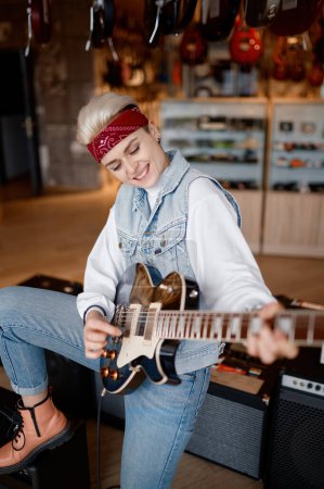 Photo for Hipster woman playing guitar connected to stereo sound amplifier feeling satisfaction and admiration of sound - Royalty Free Image