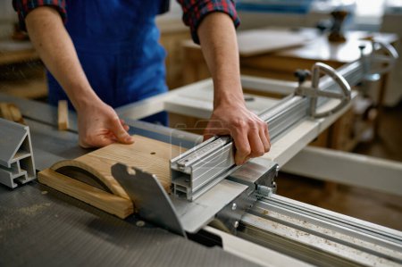 Foto de Primer plano del carpintero profesional masculino que corta el tablero de madera en el banco de trabajo circular de la sierra en taller - Imagen libre de derechos