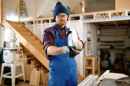 Téléchargez les photos : Homme charpentier portant des salopettes préparant la lame de scie ronde pour le remplacement. Travail du bois au concept d'atelier - en image libre de droit