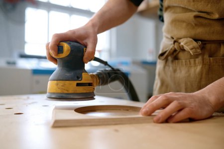Foto de Primer plano manos de artesano que trabajan con rectificadora excéntrica en taller de carpintería. Proceso de lijado orbital - Imagen libre de derechos