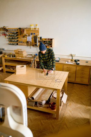 Foto de Hombre carpintero haciendo dibujo técnico con lápiz y regla sobre tabla de madera. Concepto de taller de bricolaje y carpintería - Imagen libre de derechos