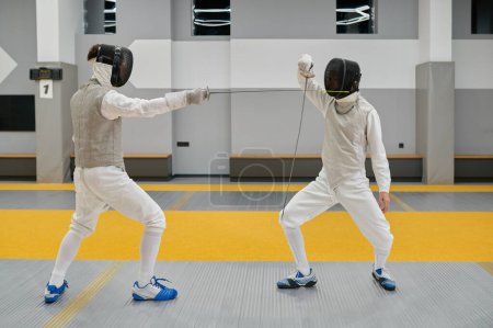 Two concentrated swordsmen wearing uniform and protective mask exercising and fighting with rapiers during fencing competition