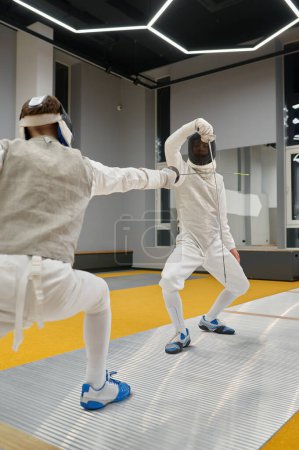 Photo for Two concentrated swordsmen wearing uniform and protective mask exercising and fighting with rapiers during fencing competition - Royalty Free Image