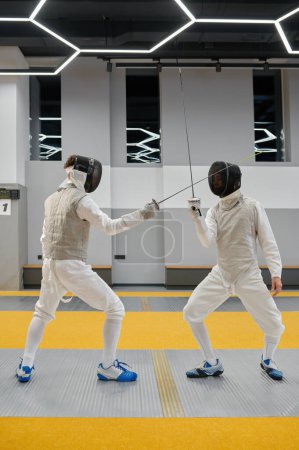 Pair of fencing partners fighting with rapiers practicing attack and defense combination during lesson at martial art club
