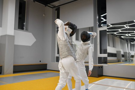 Foto de Dos esgrimistas que ejercen movimientos en duelo en la sala de esgrima de la escuela profesional de artes marciales - Imagen libre de derechos