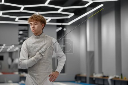 Photo for Portrait of teenager fencer wearing white fencing costume standing with sword. Preparation for competition with rapier - Royalty Free Image